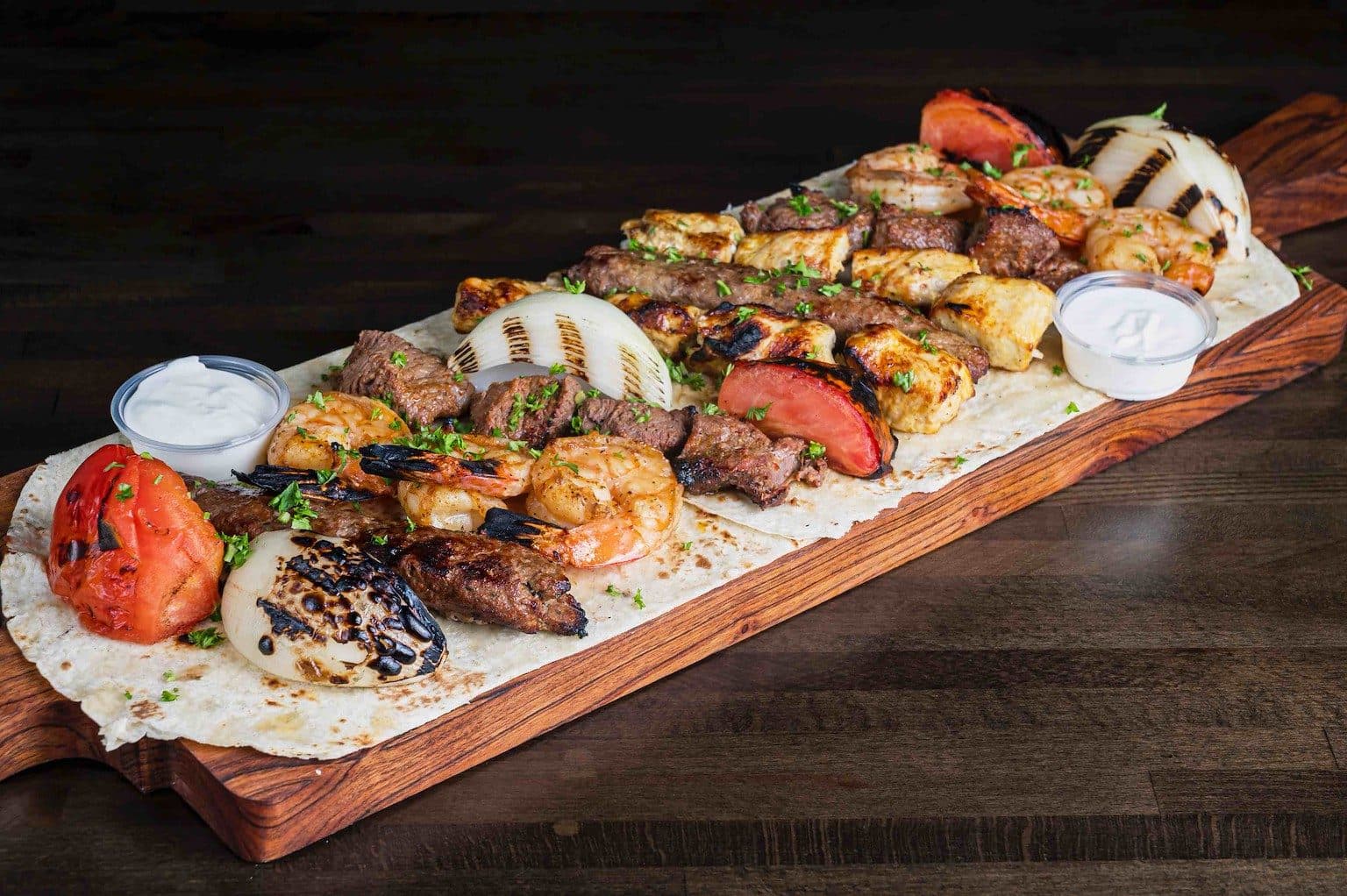 The Family Style mashawi board — kabobs, kafta, shrimp and grilled vegetables piled over saj bread
