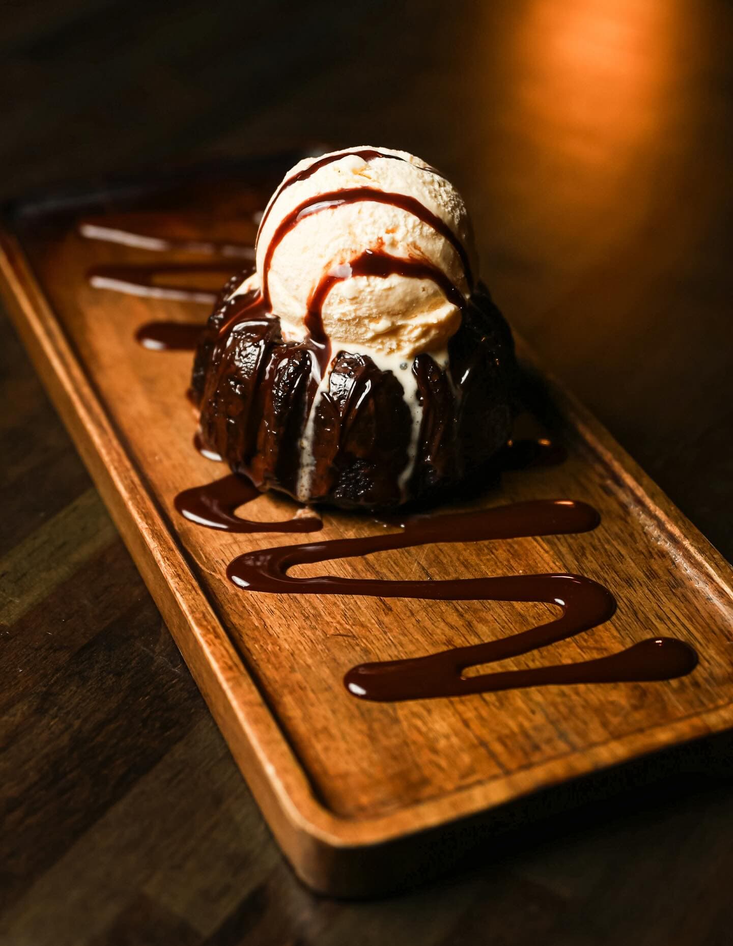 A molten chocolate cake under a scoop of vanilla, chocolate drizzled across the board
