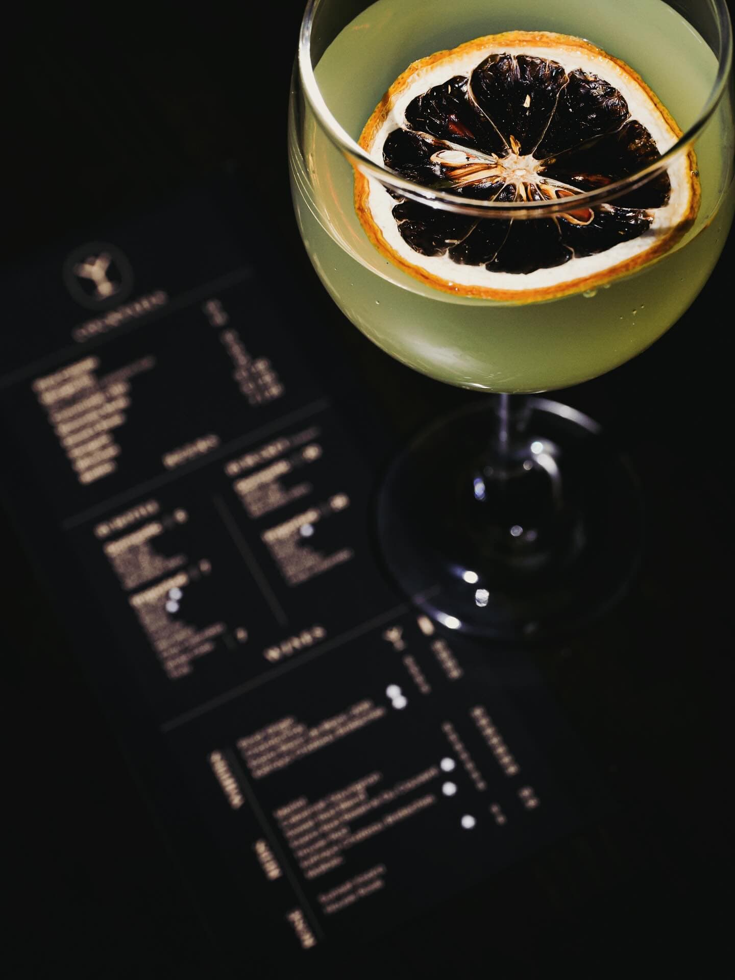 A cocktail with a dried citrus wheel, served over the drinks menu