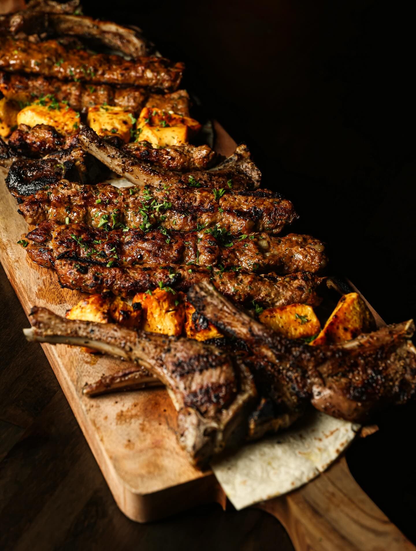 A mixed grill board off the charcoal — kafta, lamb chops and saffron chicken over saj bread